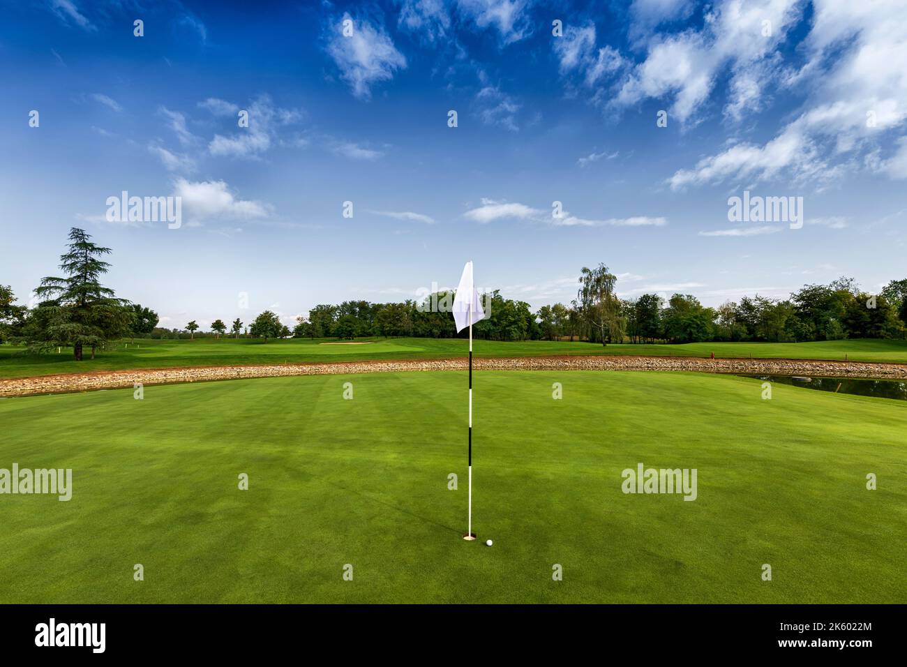 Kleiner Ball in der Nähe des Lochs mit weißer Flagge, die Position auf dem grünen Grasfeld des Golfclubs zeigt Stockfoto