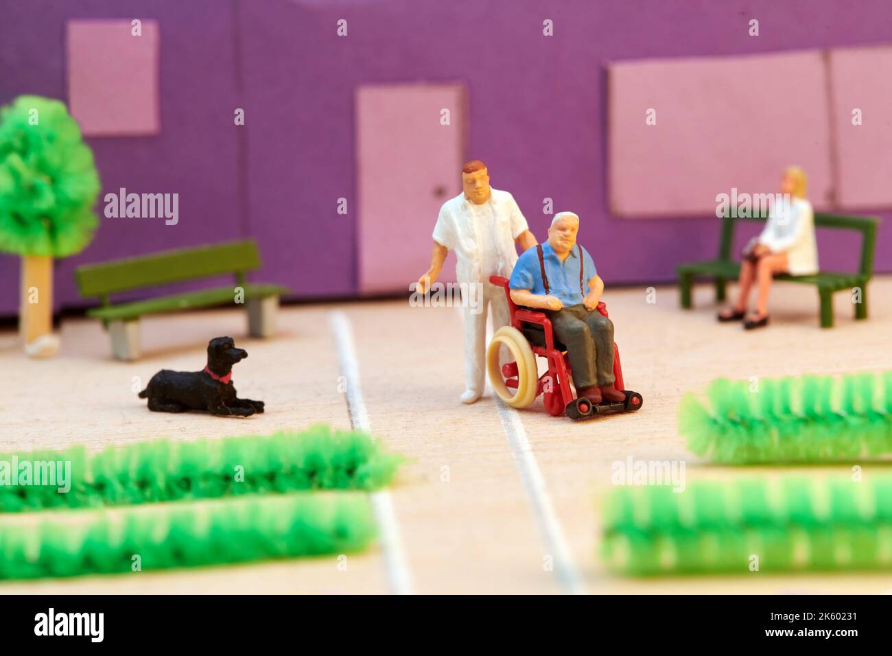 Kunststoff-Miniatur-Krankenschwester in Uniform hilft älteren Patienten auf Rollstuhl vor dem Hospiz Gebäude Stockfoto