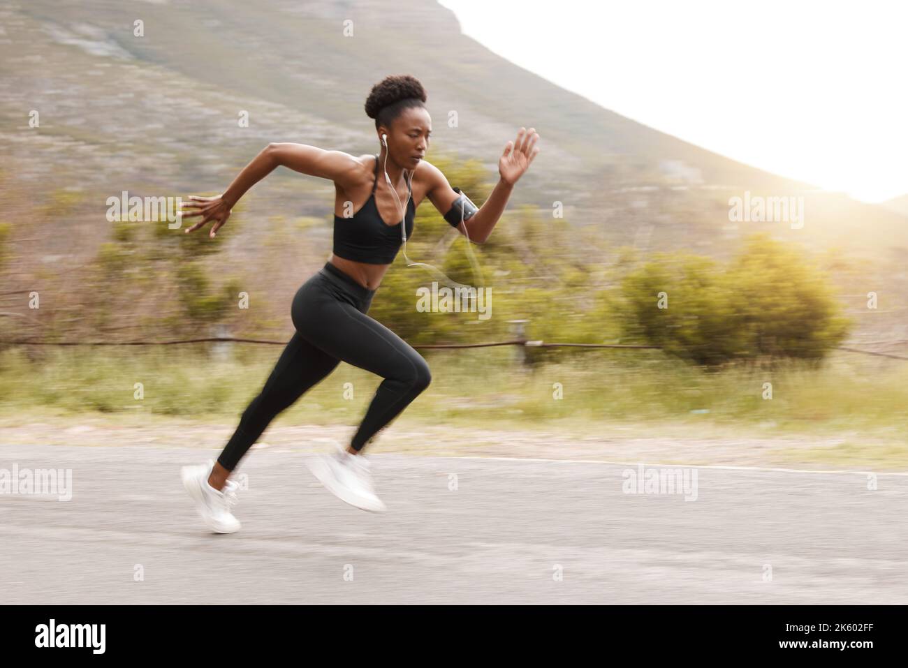 Motion Blur Full Body Fit aktive afroamerikanische Frau läuft schnell, während sie draußen in der Natur trainiert. Starke sportliche schwarze Frau sprintet während Stockfoto