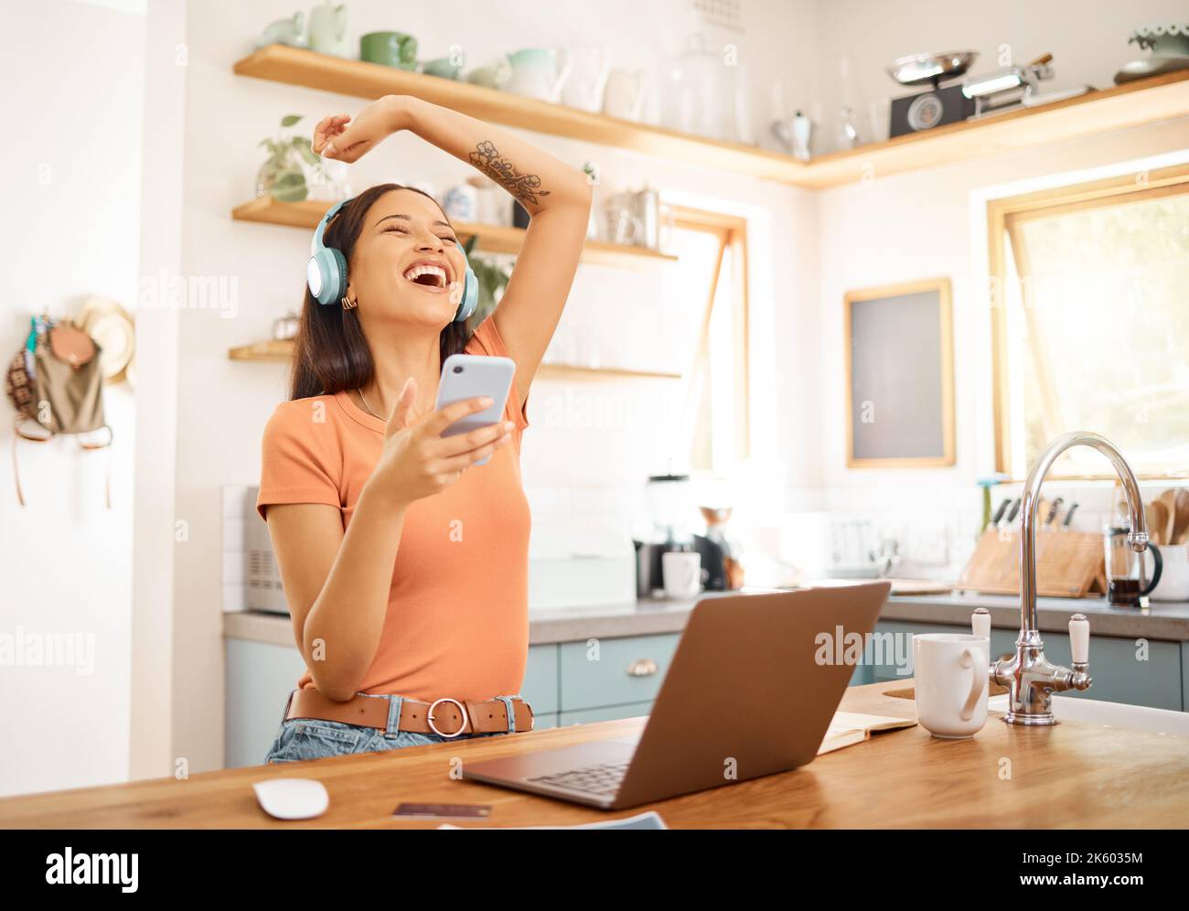 Junge schöne glückliche gemischte Rennen Geschäftsfrau hält und mit einem Telefon, während sie Kopfhörer trägt und Musik von zu Hause aus hört. Eine Freude Stockfoto