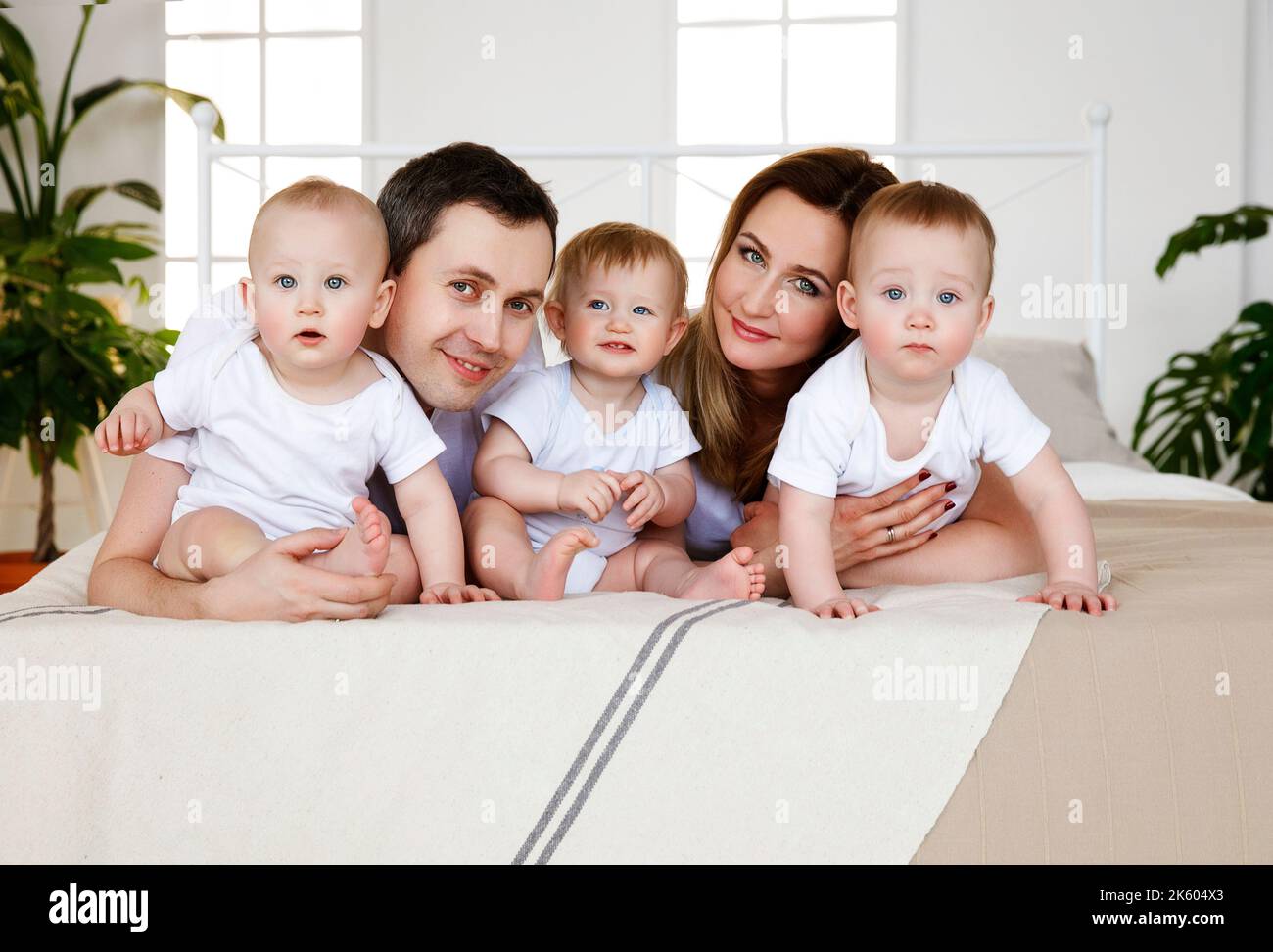 Portrait, große Familie, mit Drillingen auf dem Bett. Eltern und kleine Kinder. Medizin, Öko Stockfoto