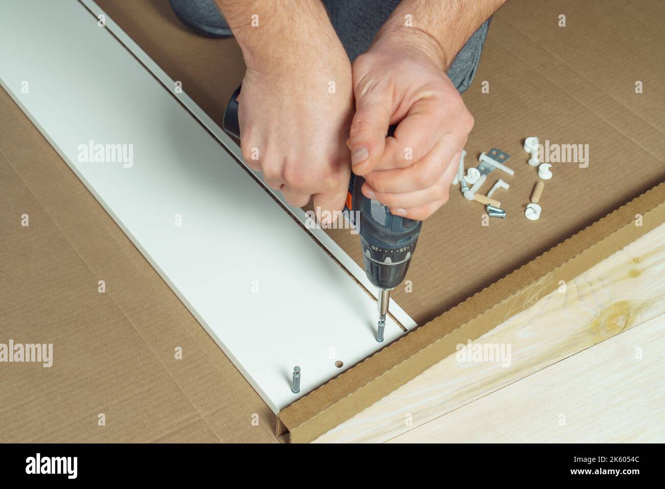 Männliche Hände halten schnurlosen elektrischen Schraubendreher, Schraube, um Wände der weißen Schublade zu befestigen, Montage Kommode oder Kleiderschrank auf dem Boden. Selbstmontage von Möbeln Stockfoto