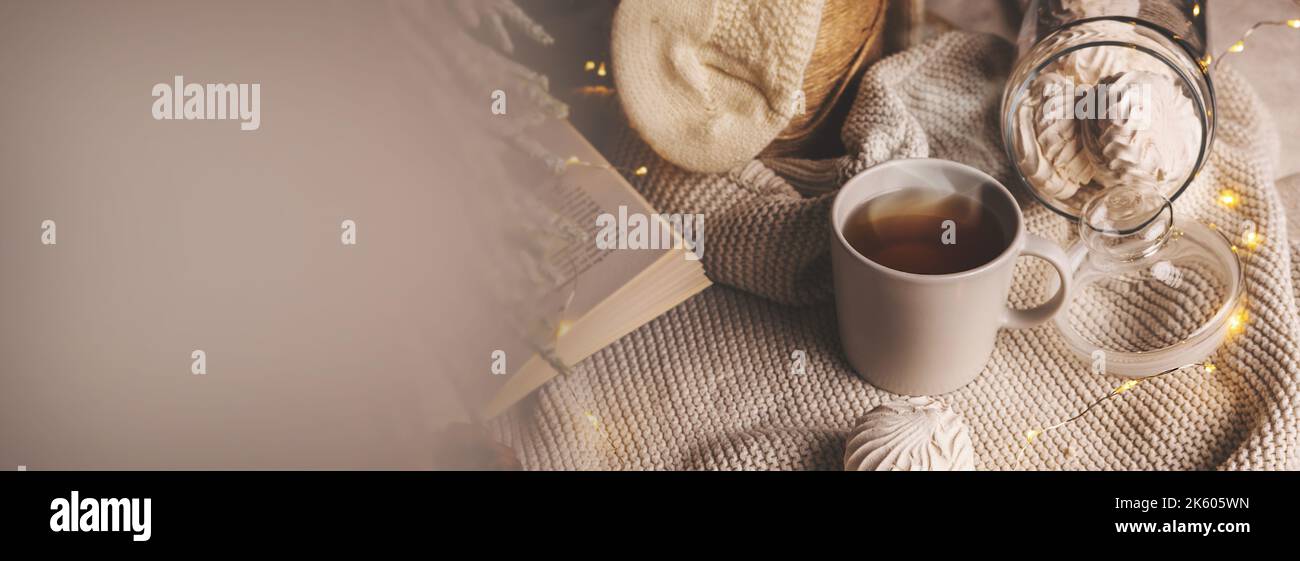 Gemütliche Winterkomposition mit einer Tasse Tee, Süßigkeiten und weihnachtslichtern auf Strickdecke. Banner mit Kopierfläche Stockfoto