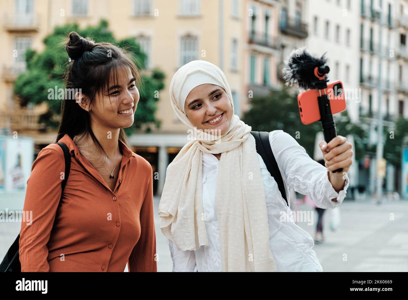 Multiethnische Freundinnen, die lächeln, während sie mit einem Mobiltelefon im Freien auf der Straße streamen oder aufzeichnen. Stockfoto