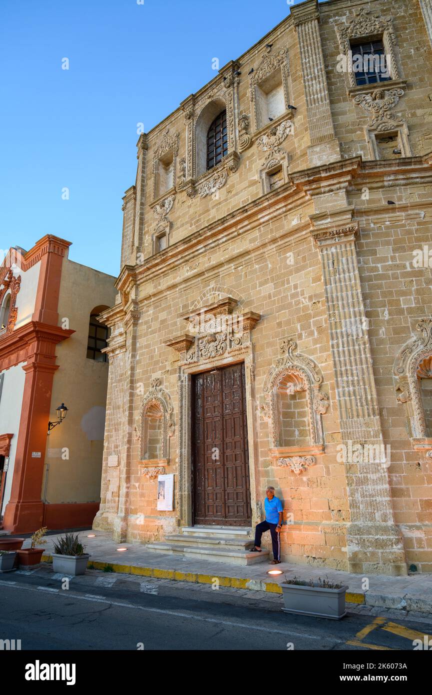 Ein älterer Mann, der vor der Kirche San Domenico al Rosario in der Altstadt von Gallipoli, Apulien (Apulien), Italien, bei warmem Abendsonne steht. Stockfoto