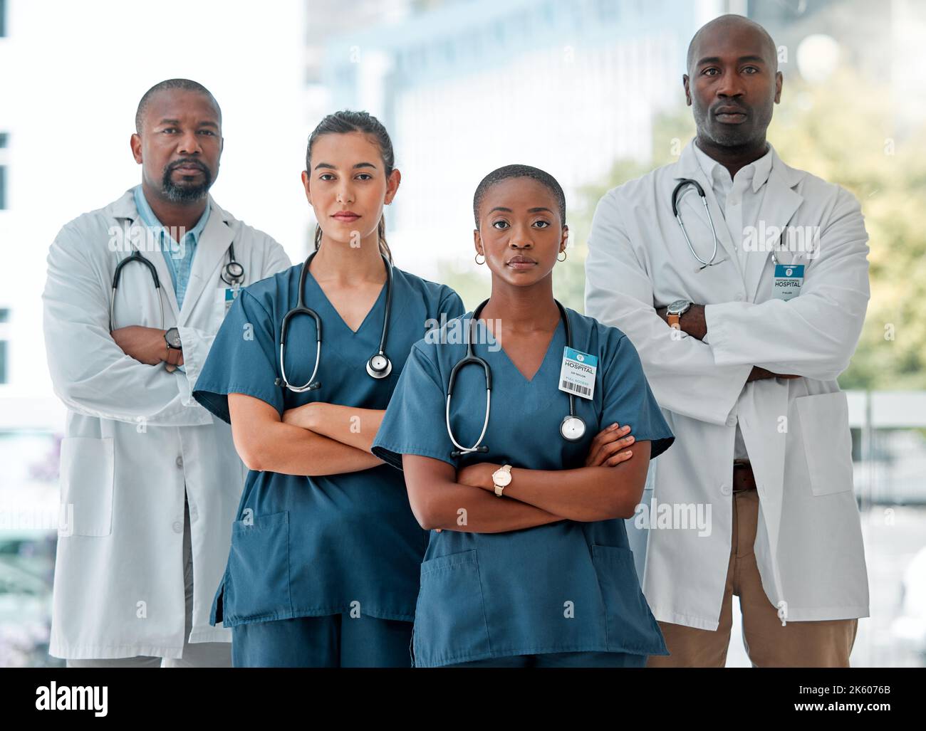 Eine Gruppe ernsthafter verschiedener Ärzte, die in einer Reihe mit gekreuzten Armen stehen, während sie in einem Krankenhaus arbeiten. Fokussierte medizinische Fachkräfte bei der Arbeit Stockfoto