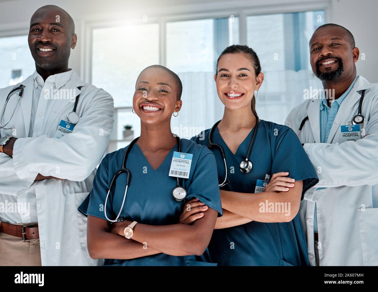 Eine Gruppe glücklicher Ärzte, die bei der Arbeit in einem Krankenhaus mit gekreuzten Armen stehen. Professionelle medizinische Fachkräfte, die lächeln und bei der Arbeit stehen Stockfoto
