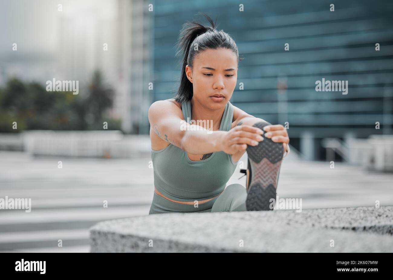 Sportliche junge hispanische Athletin, die ihre Beine vor einem Lauf nach draußen streckt. Fit junge Frau Aufwärmen während des Trainings in der Stadt. Übung ist Stockfoto