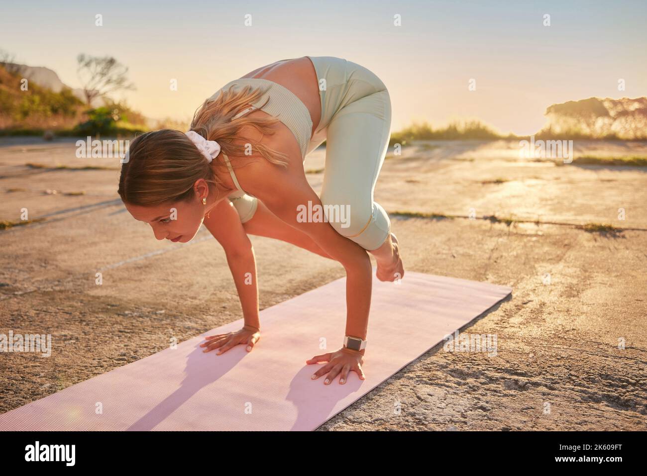 Yoga-Frau in voller Länge in Krähenhaltung in der Praxis im Freien in der entlegenen Natur. Schöne kaukasische Person mit Matte, balanciert auf den Händen, während Stockfoto