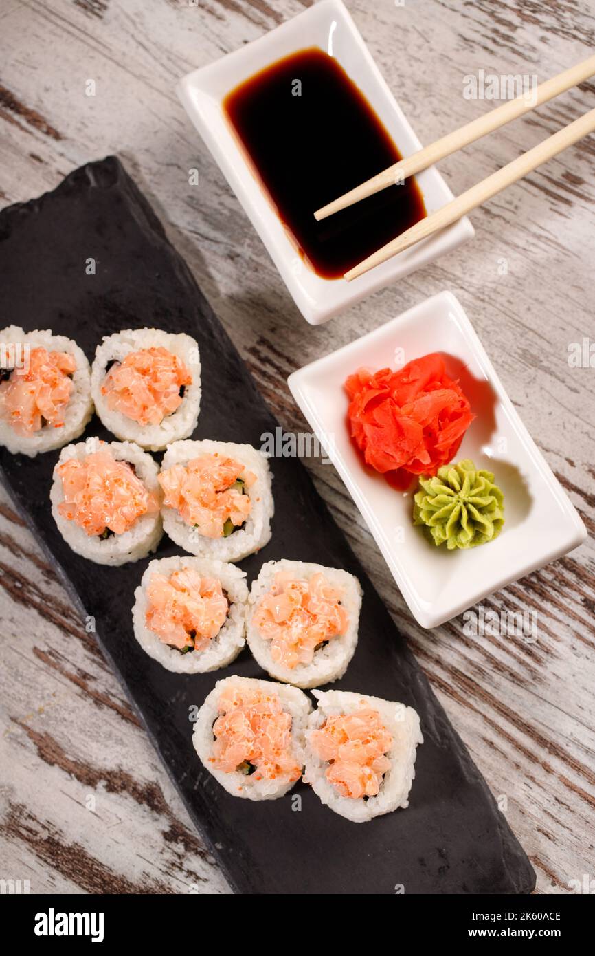 Serviert in japanischem Stil. Sushi-Rolle mit gehacktem Lachs und Kaviar wird auf rechteckigem schwarzem Schiefer serviert. Draufsicht auf Sushi-Rolle auf dem Tisch Stockfoto