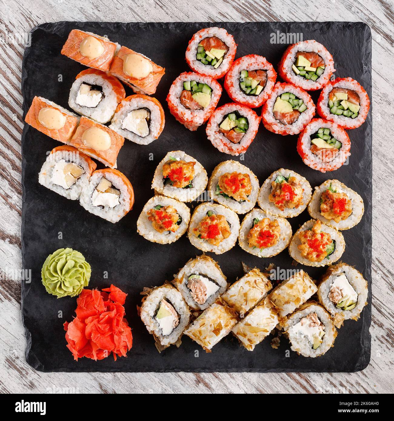 Asiatische Küche. Ein großes Sushi-Set aus verschiedenen Sushi-Rollen wird auf schwarzem quadratischem Metallschiefer serviert. Blick von oben auf verschiedene Brötchen mit verschiedenen frischen Ingeredi Stockfoto