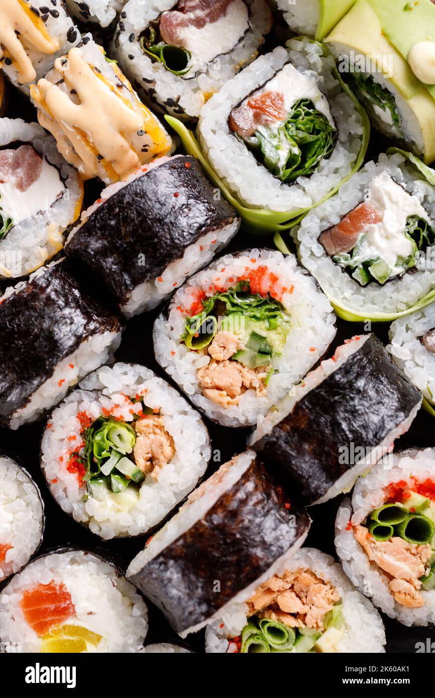 Nahaufnahme verschiedener Sushi-Rollen mit verschiedenen Füllungen auf schwarzem Metallschiefer. Sushi-Set mit Lachs, rotem Kaviar, Käse, Gurke, Avocado und SE Stockfoto