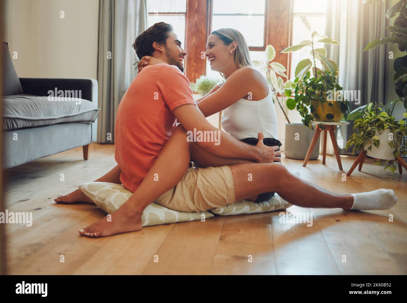 Glückliches kaukasisches Paar, das liebevoll ist und einen romantischen, intimen Moment genießt, während es auf dem Wohnzimmerboden sitzt. Junge Frau sitzt auf Stockfoto
