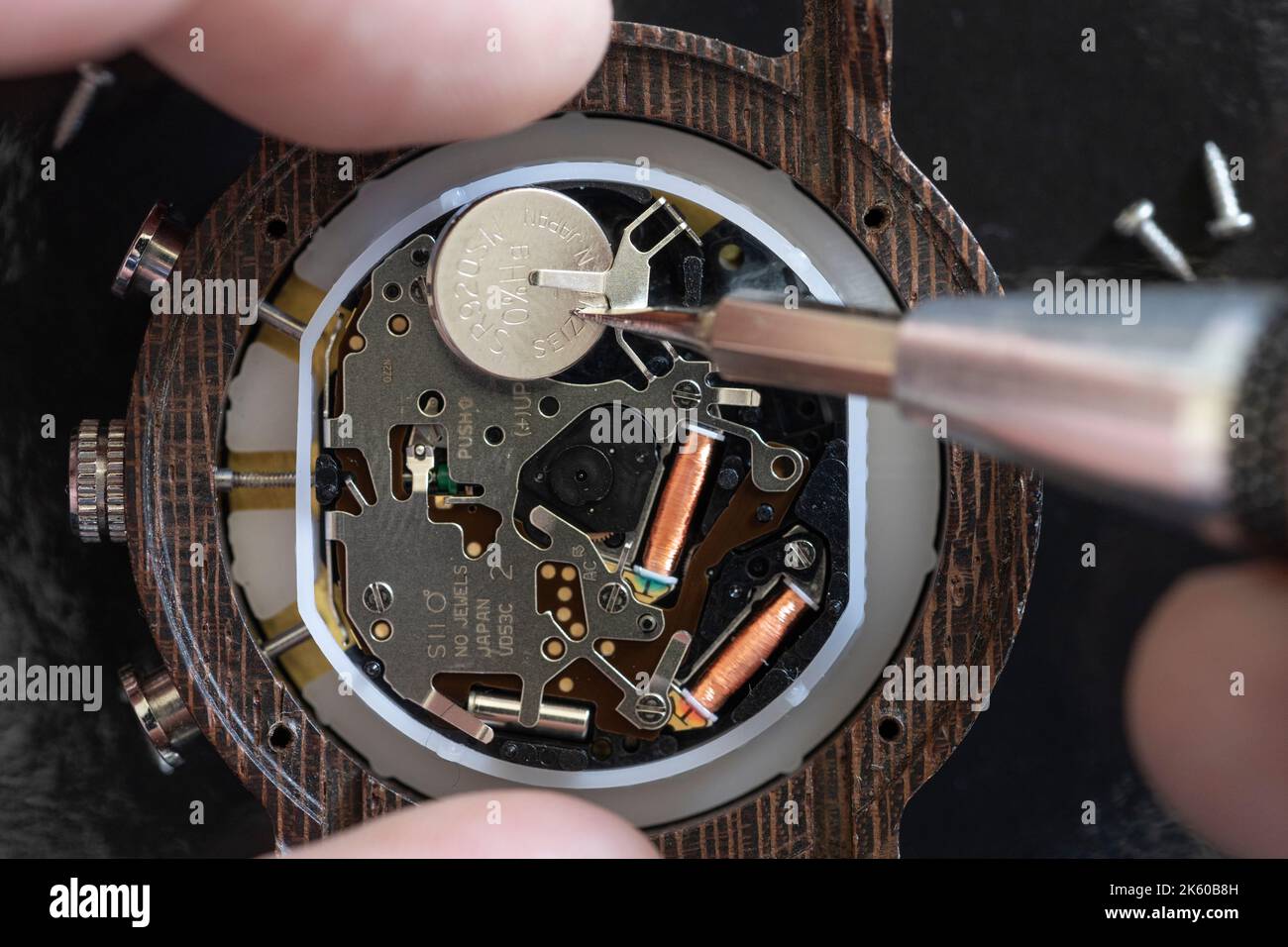 Makro-Nahaufnahme eines Mannes, der einen Mini-Schraubendreher verwendet, um eine Batterie für eine Armbanduhr zu Hause zu ersetzen, wobei das Innenleben der Uhr freigelegt ist. England Stockfoto