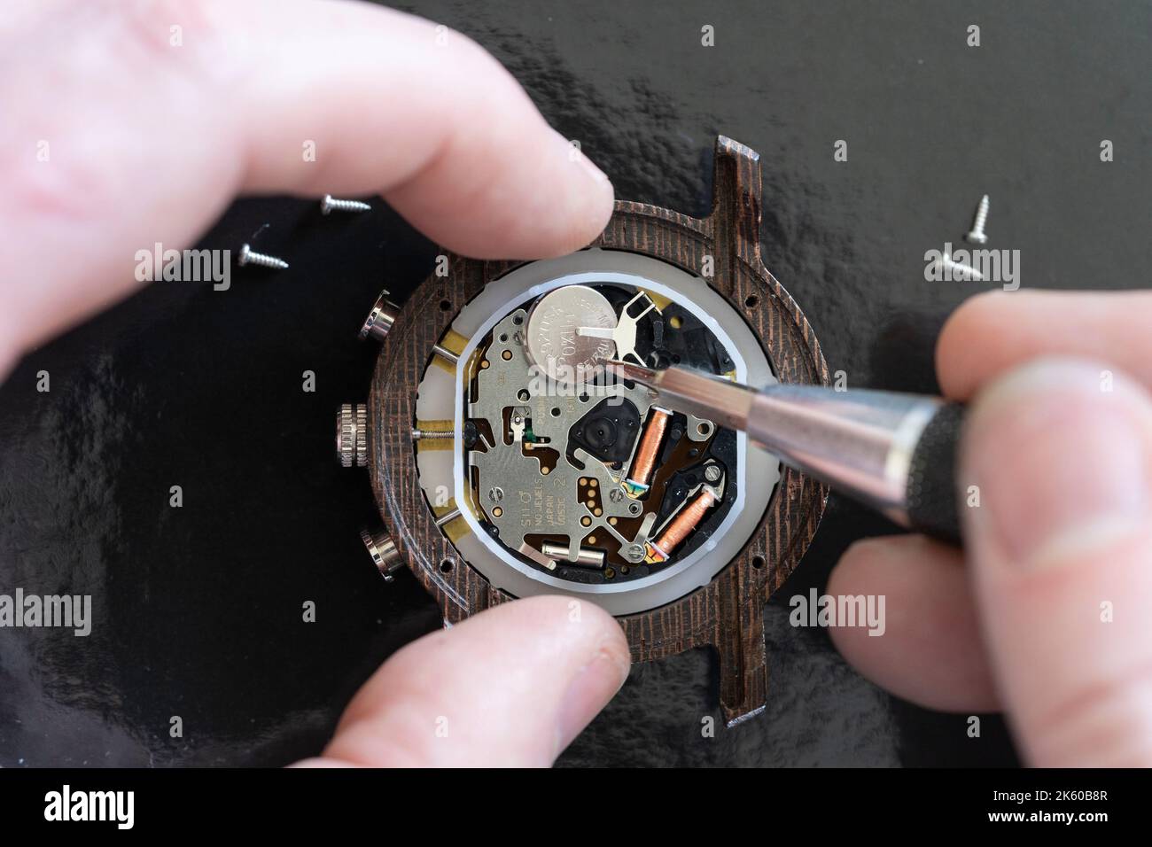 Makro-Nahaufnahme eines Mannes, der einen Mini-Schraubendreher verwendet, um eine Batterie für eine Armbanduhr zu Hause zu ersetzen, wobei das Innenleben der Uhr freigelegt ist. England Stockfoto