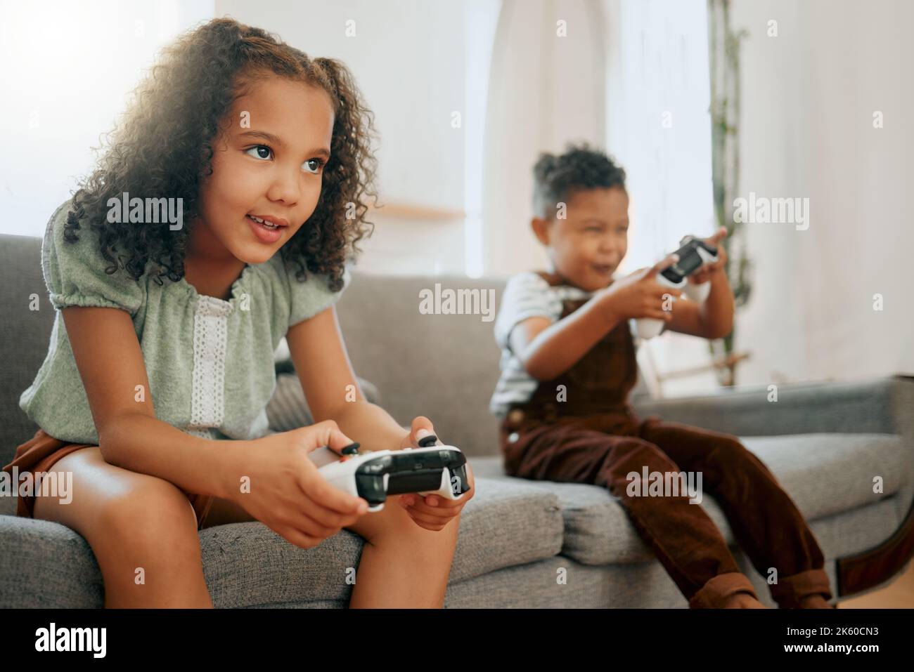 Zwei glückliche Geschwister aus gemischtem Rennen entspannen sich auf dem Loungesofa, während sie lustige Videospiele spielen. Kinder spielen nur während sie zu Hause spielen Stockfoto