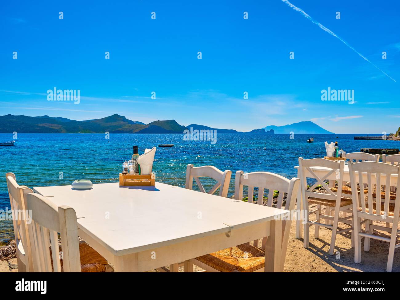 Weiße Stühle und Tische der griechischen Taverne am Wasser am Tag. Urlaub, Griechenland, Sommer, Restaurant, Essen im Freien, inseln, Hafen, Yachthafen, Yachten Stockfoto