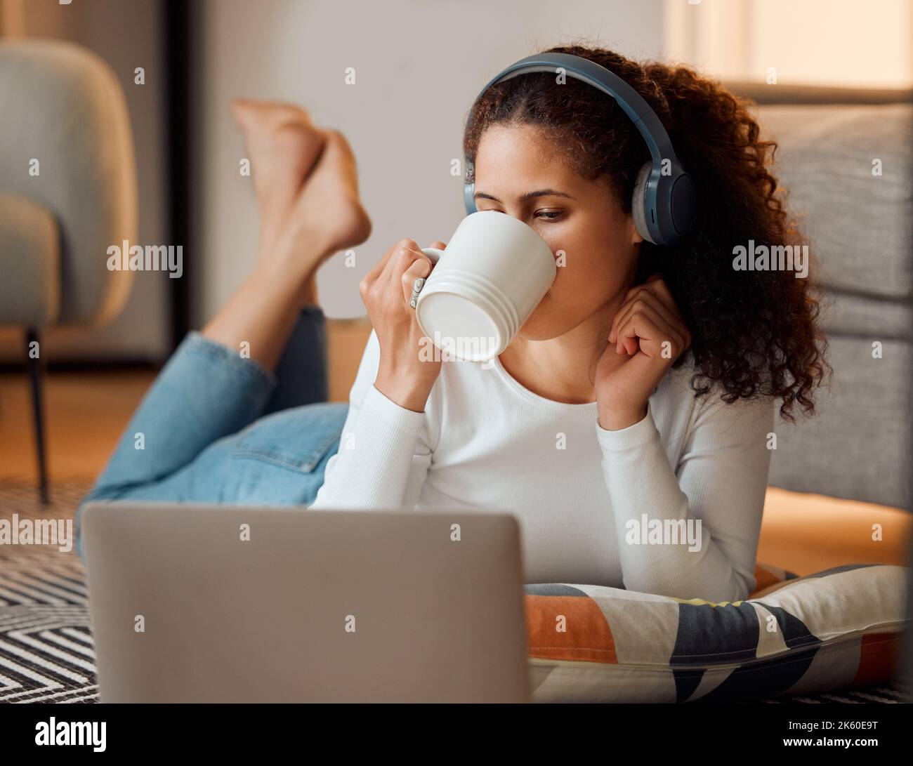 Frau nutzt das Internet auf ihrem Laptop. Junge Frau trinkt Tee und hört Musik. Junges Mädchen genießt eine Tasse Kaffee mit ihrem Laptop. Frau Stockfoto