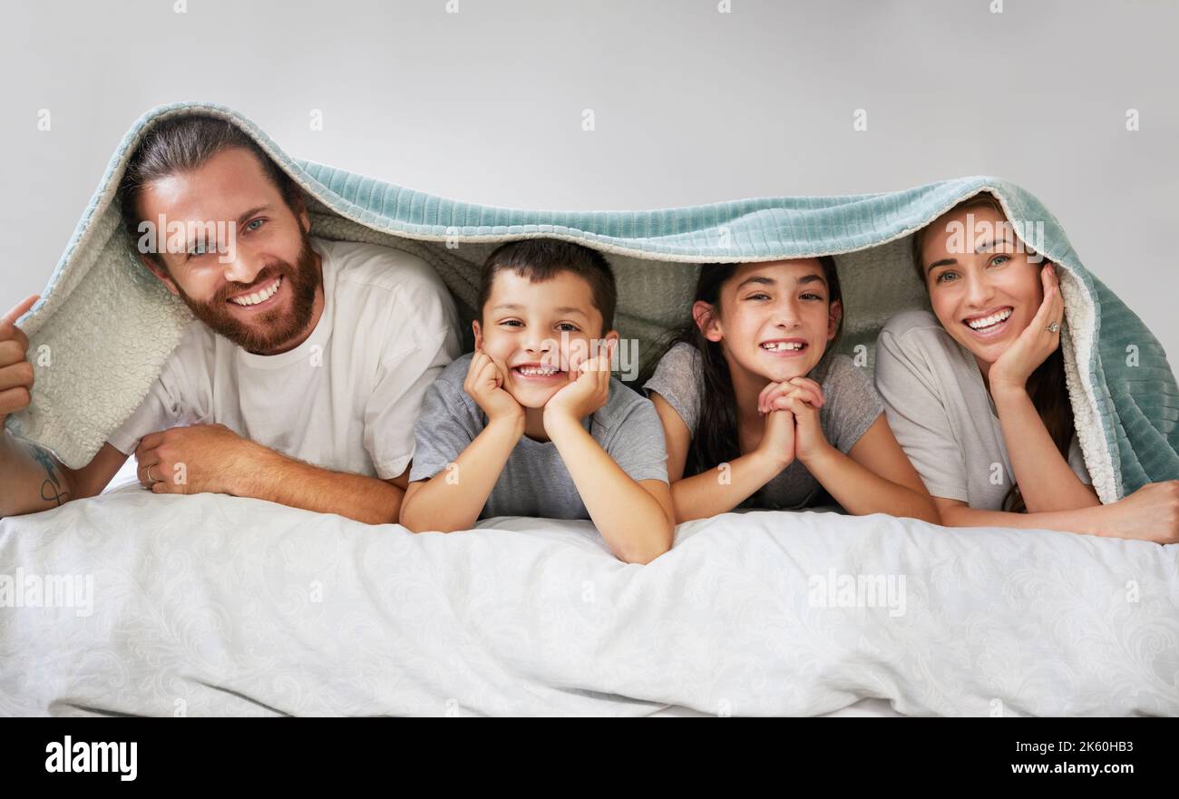 Porträt einer glücklichen vierköpfigen kaukasischen Familie, die in einer Reihe auf einem Bett mit einer Fleecedecke über dem Kopf liegt. Sorglose Eltern verbringen Freizeit mit Stockfoto
