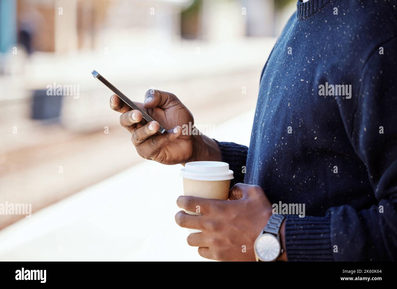 Nahaufnahme eines schwarzen Geschäftsmannes, der unterwegs ist und auf einen Zug wartet, während er ein Handy benutzt und eine Tasse Kaffee trinkt. afroamerikanischer Mann mit einem Stockfoto