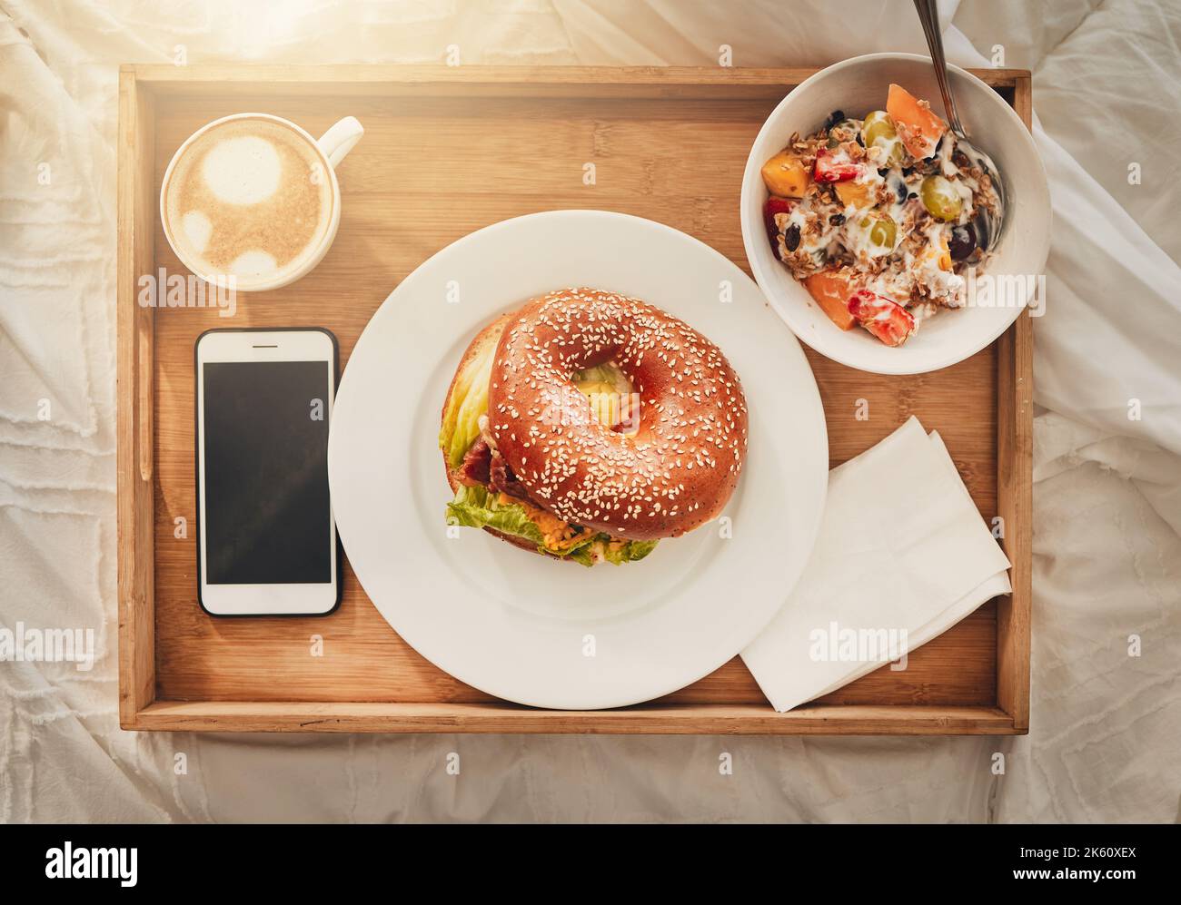 Das perfekte Geschenk zum Muttertag. Ein Tablett mit einem ausgewogenen Frühstück, einem Bagel, Kaffee und einem Handy. Alles, was man zum Frühstück im Bett braucht Stockfoto