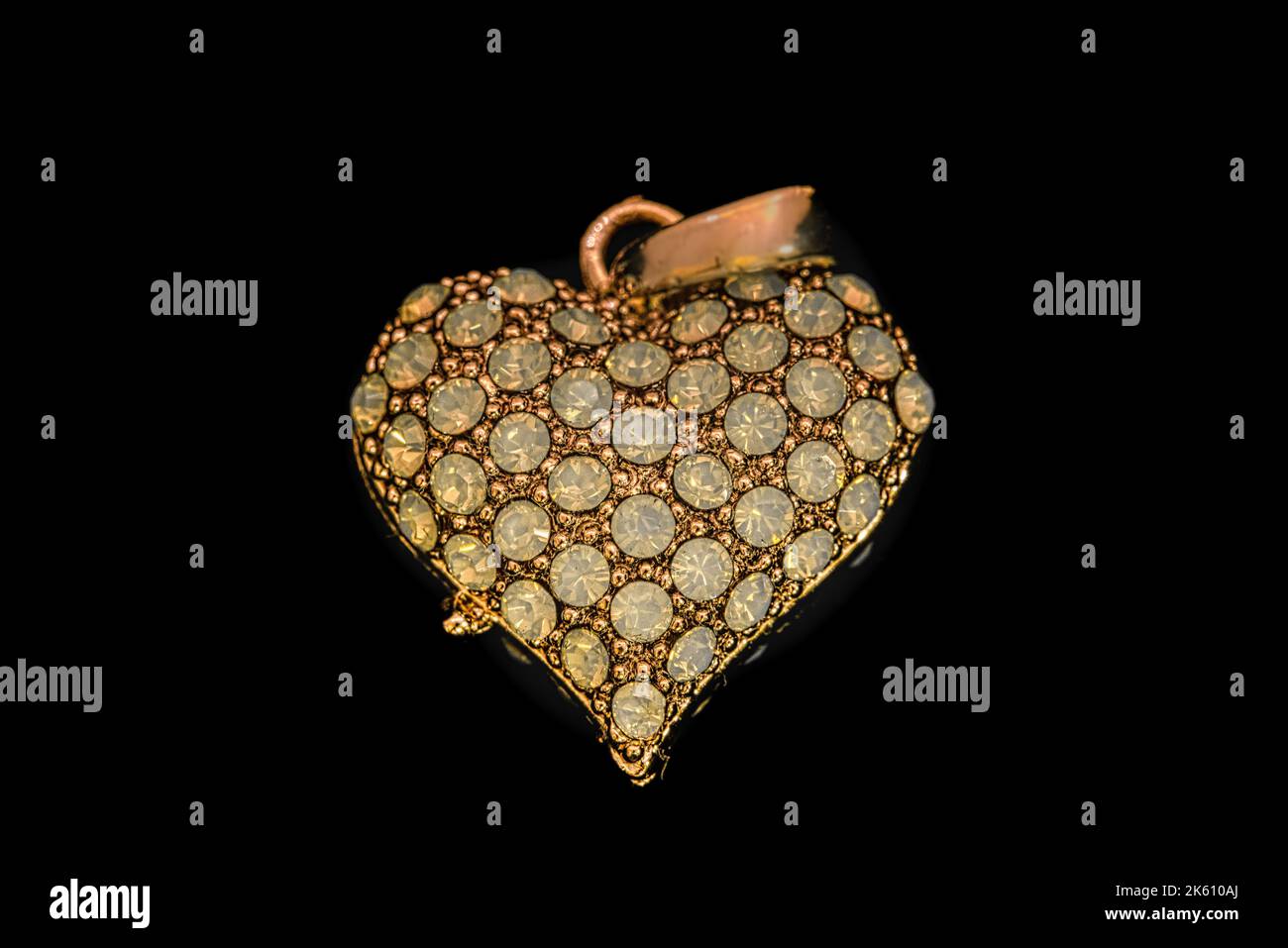 Eine Nahaufnahme eines funkelnden goldenen Herz-Anhänger-Charms auf schwarzem Hintergrund Stockfoto