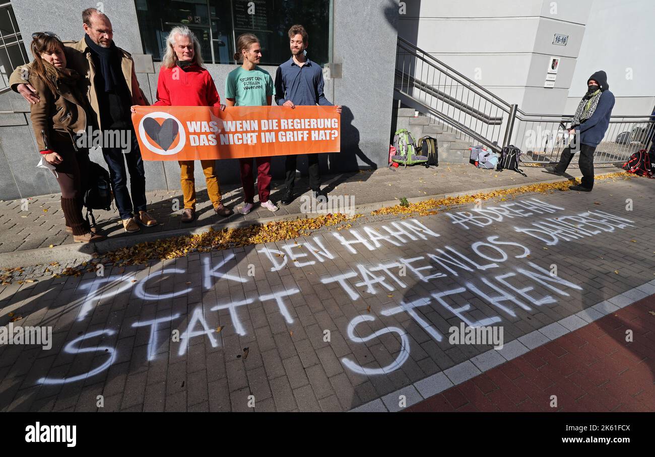 11. Oktober 2022, Mecklenburg-Vorpommern, Neubrandenburg: Vor Beginn des Prozesses stehen Mitglieder und Sympathisanten der Gruppe "Letzte Generation" vor dem Landgericht mit einem Transparent mit der Aufschrift "Was, wenn die Regierung damit nicht umgehen kann?". In der Mitte trägt Raúl Semmler ein T-Shirt mit der Aufschrift „Stoppt den Wahnsinn der fossilen Brennstoffe!“ Auf dem Bürgersteig im Vordergrund steht: „Den Wasserhahn von PCK ausschalten, anstatt untätig dazustehen“. Im Zivilfall geht es darum, ob die PCK Schwedt Raúl Semmler verbieten kann, Fotos von der Besetzung von Pumpstationen im zu verteilen Stockfoto