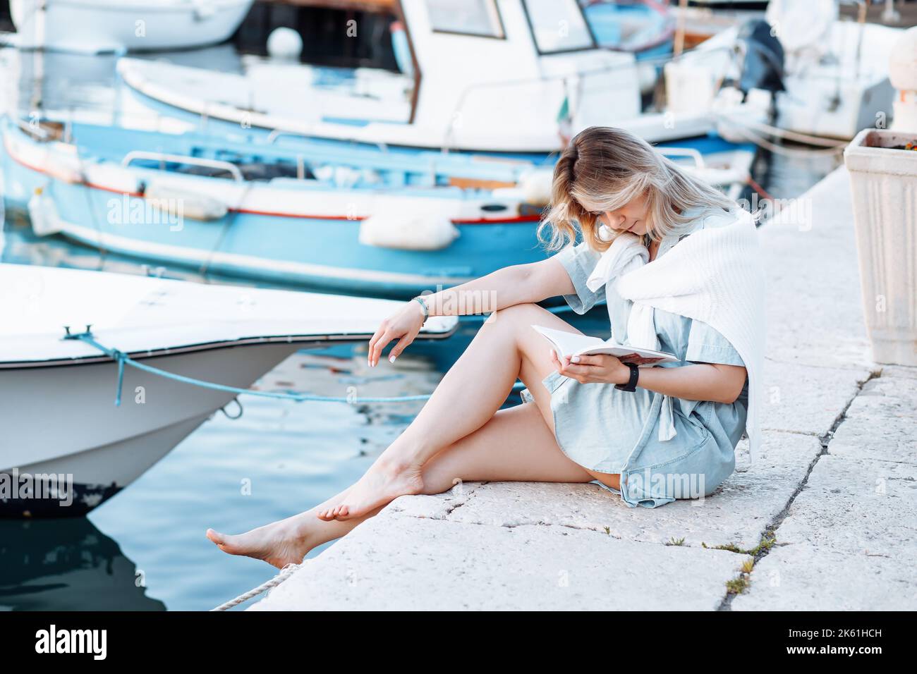 Bootsfahrten auf der Yacht. Attraktive blonde in Denim Jumpsuit Farbe von Meerwasser ist sorgfältig Buch lesen. Sport, Tourismus. Stockfoto