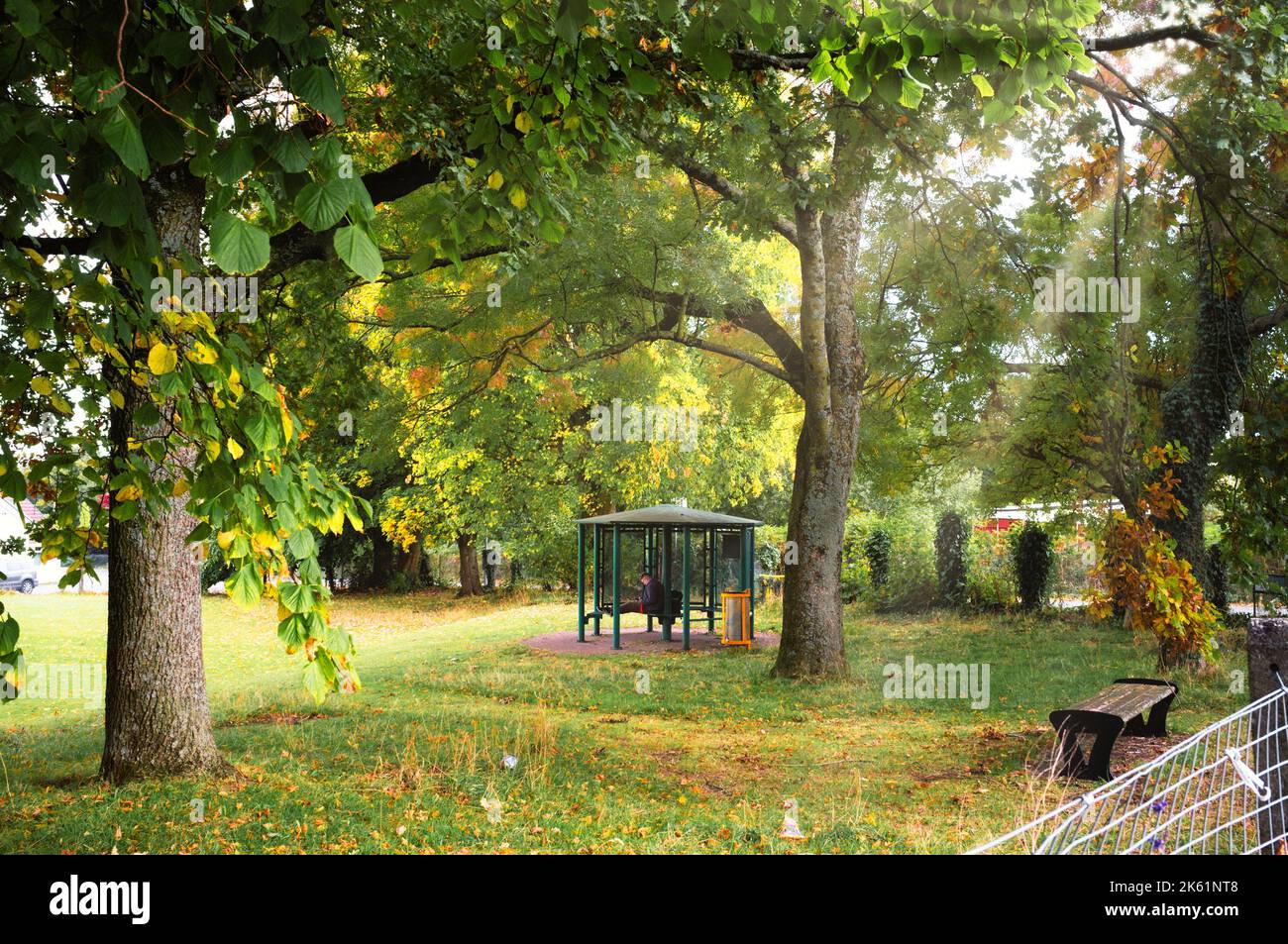 Ein junger Mann sitzt in einem geschützten Bereich in einem Park. Künstlerische Ergänzung durch Sonnenlicht. Stockfoto