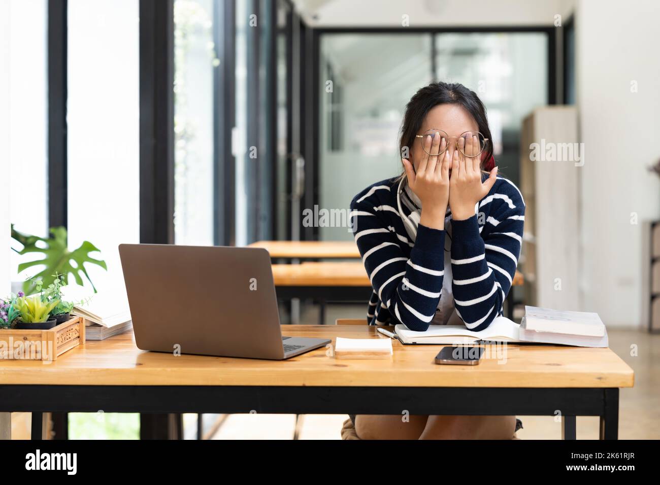 Müde asiatische männliche Student sitzen am Schreibtisch mit Laptop. Gelangweilte Jugendliche sind erschöpft von der Vorbereitung auf Tests oder dem Schreiben von Kursarbeiten und fühlen sich müde Stockfoto