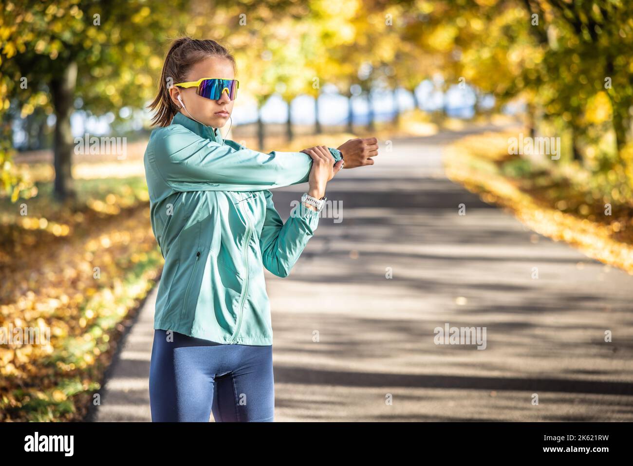 Eine junge Frau streckt an einem Herbsttag im Freien den Arm, trägt Uhren, Sonnenschutz und Kopfhörer. Stockfoto