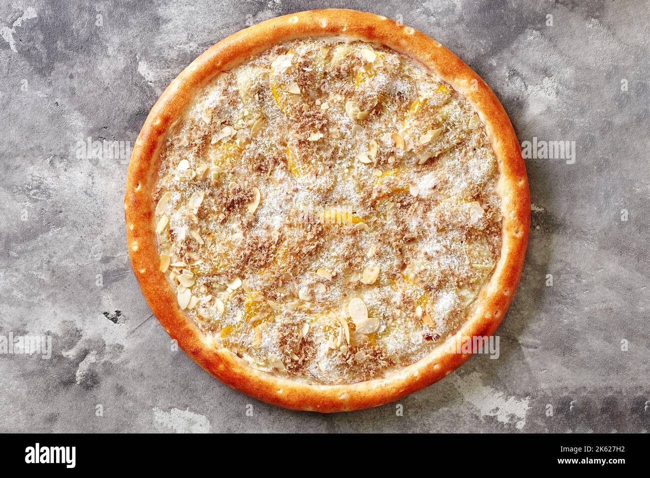 Süße Pizza mit Kondensmilch, Banane, Pfirsich, Kokosraspeln und Mandelflocken auf grauer Oberfläche Stockfoto