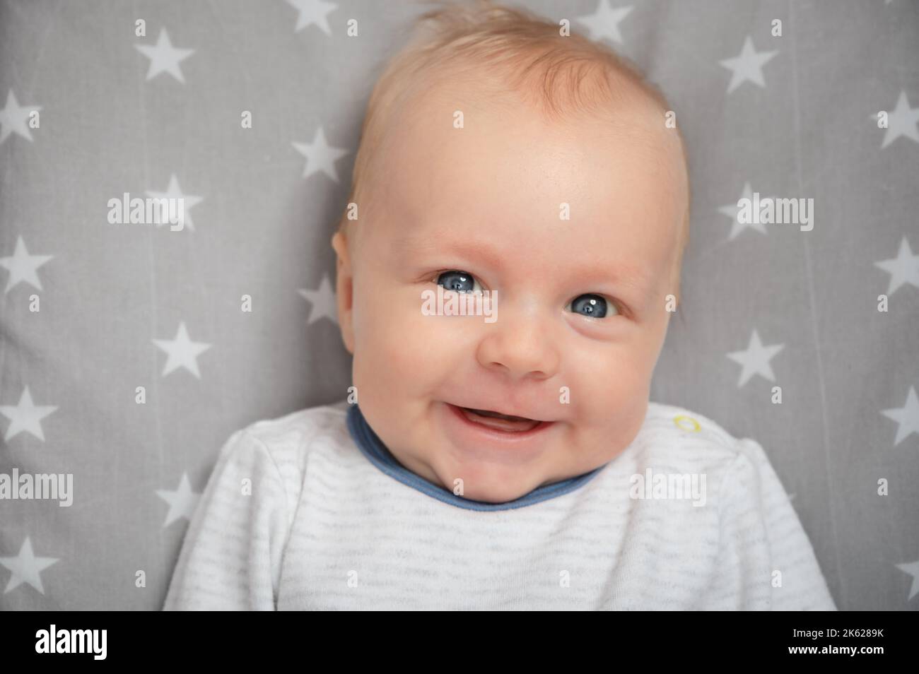 Porträt eines lächelnden Neugeborenen mit offenem Mund, Nahaufnahme. Glücklich lächelndes Kind mit blauen Augen, Blick auf die Kamera. Gesichtsausdruck. Stockfoto