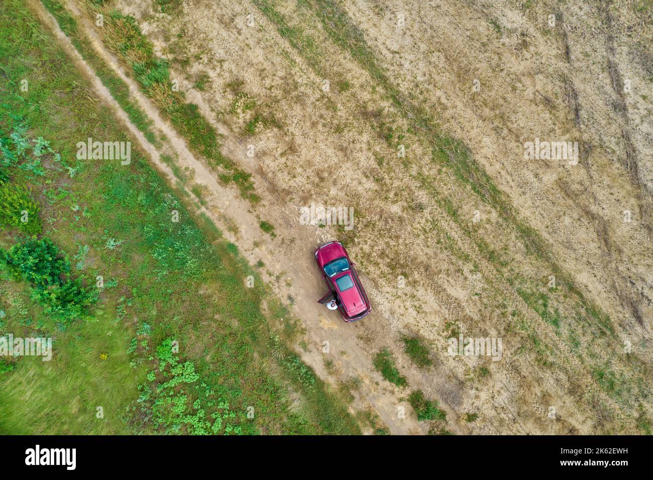 Drohne Luftaufnahme über roten SUV-Auto steht mit Fahrer auf einem geernteten Sommer landwirtschaftlichen Feld Stockfoto