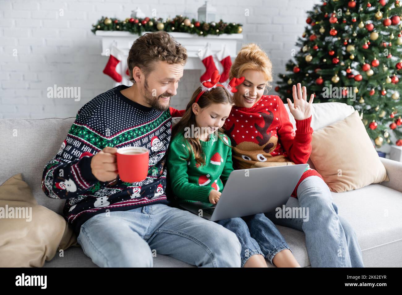 Lächelnde Familie in Neujahr Pullover mit Videoanruf auf Laptop zu Hause, Stock Bild Stockfoto