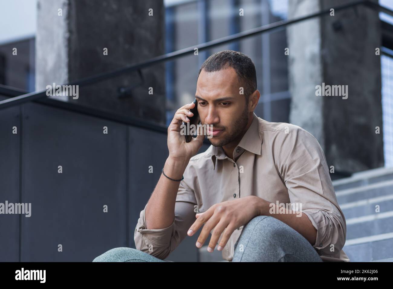 Deprimierter Mann, der auf der Treppe des Bürogebäudes sitzt, frustriert telefoniert, verärgert und entlassen Büroangestellter in legerem Hemd. Stockfoto