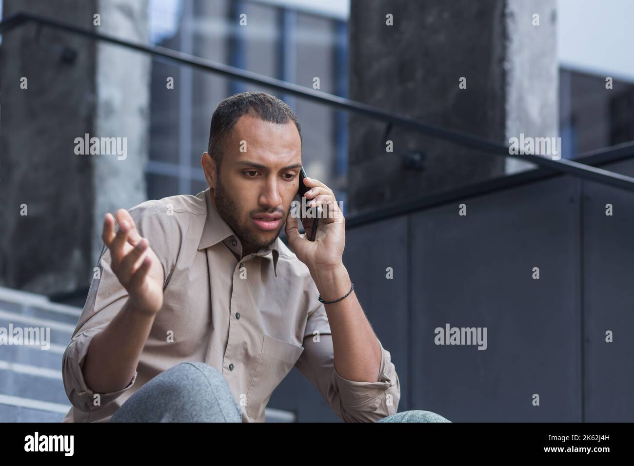 Deprimierter Mann, der auf der Treppe des Bürogebäudes sitzt, frustriert telefoniert, verärgert und entlassen Büroangestellter in legerem Hemd. Stockfoto