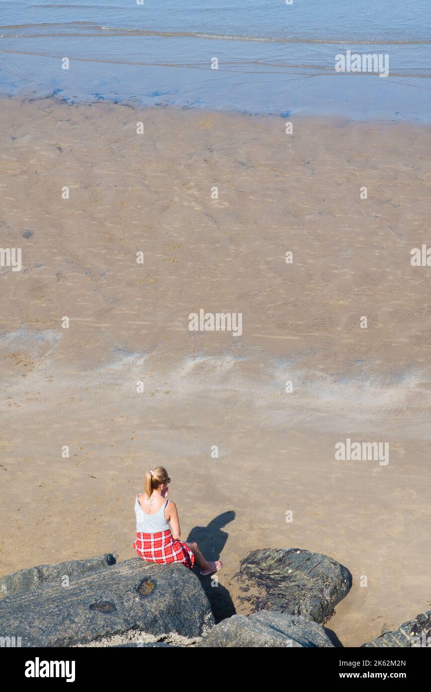 Eine Frau, die allein auf einem Felsen sitzt und auf North Bay, Scarborough, aufs Meer blickt Stockfoto