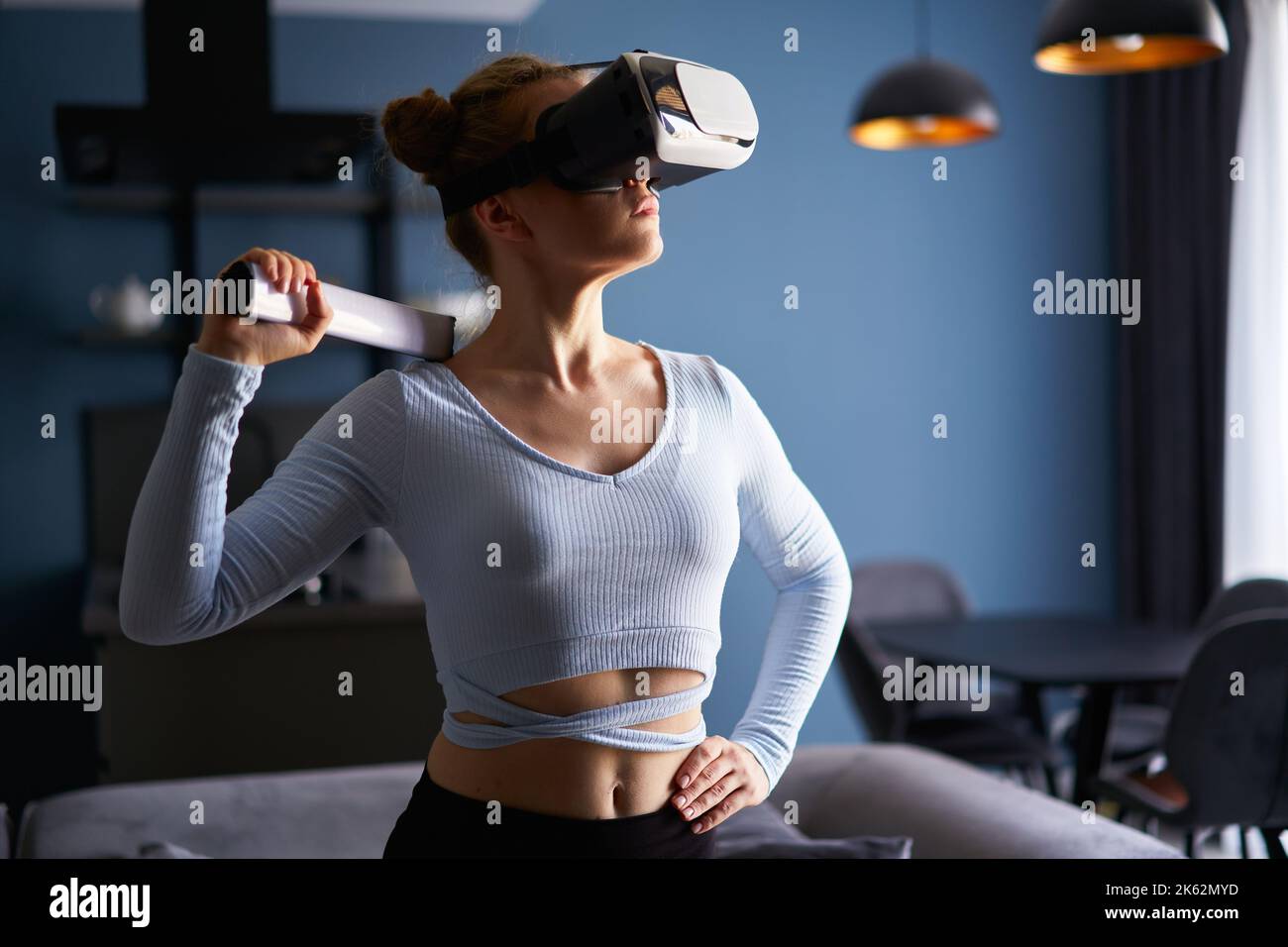 Junge futuristische blonde Mädchen trägt Virtual-Reality-Headset, halten Controller spielen ein Videospiel zu Hause. Frau spielt Avatar VR Shooting Fight Stockfoto