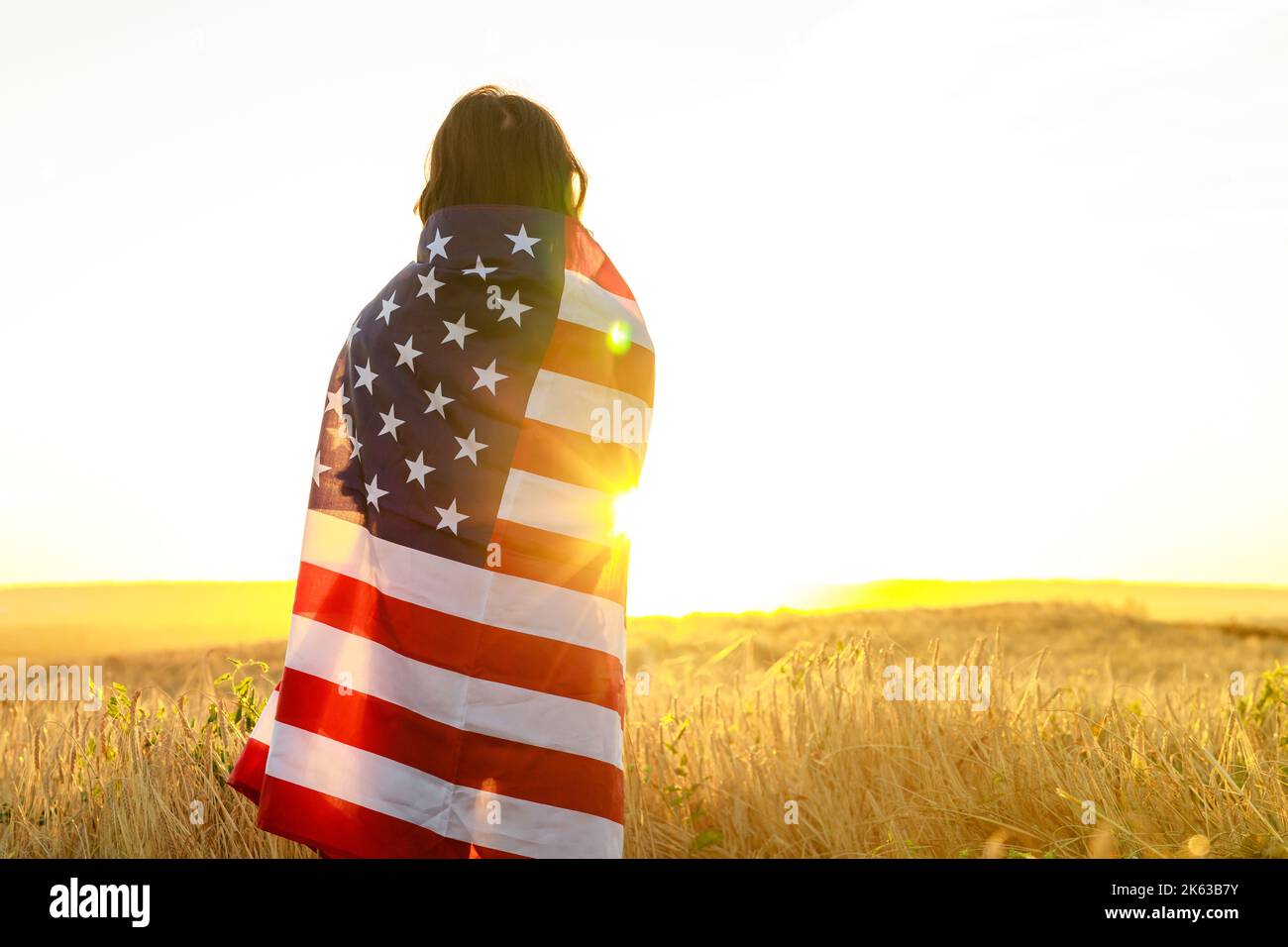 Frau auf dem Feld mit US-Sternen und Streifenflagge in der Abendsonne bei goldenem Sonnenuntergang Stockfoto