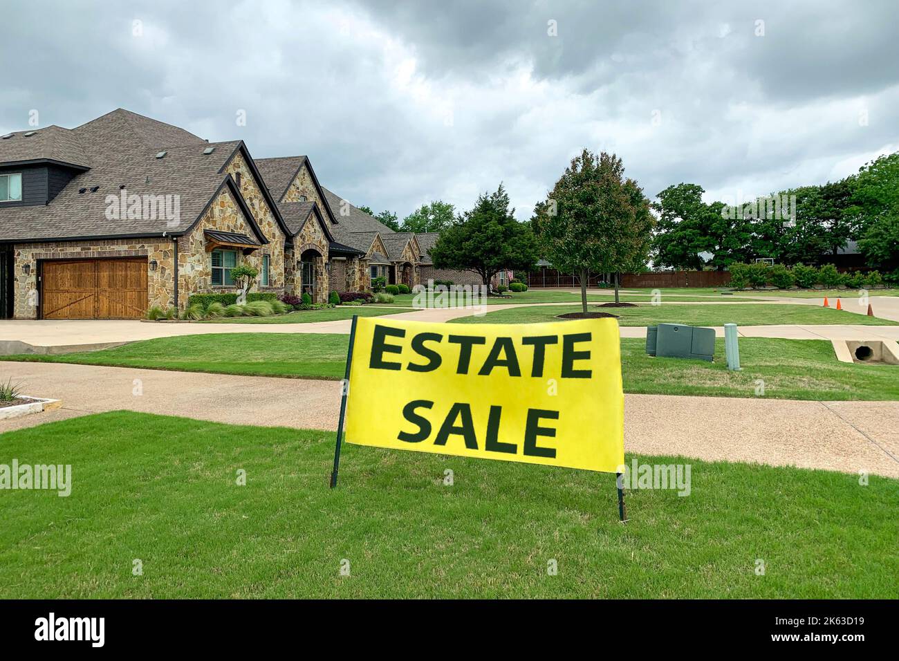 Außenaufnahme eines Wohnhauses mit Straße und gepflegtem Rasen davor, großes gelbes Schild mit Immobilienverkauf Inschrift. Verkauf von Villen. Stockfoto