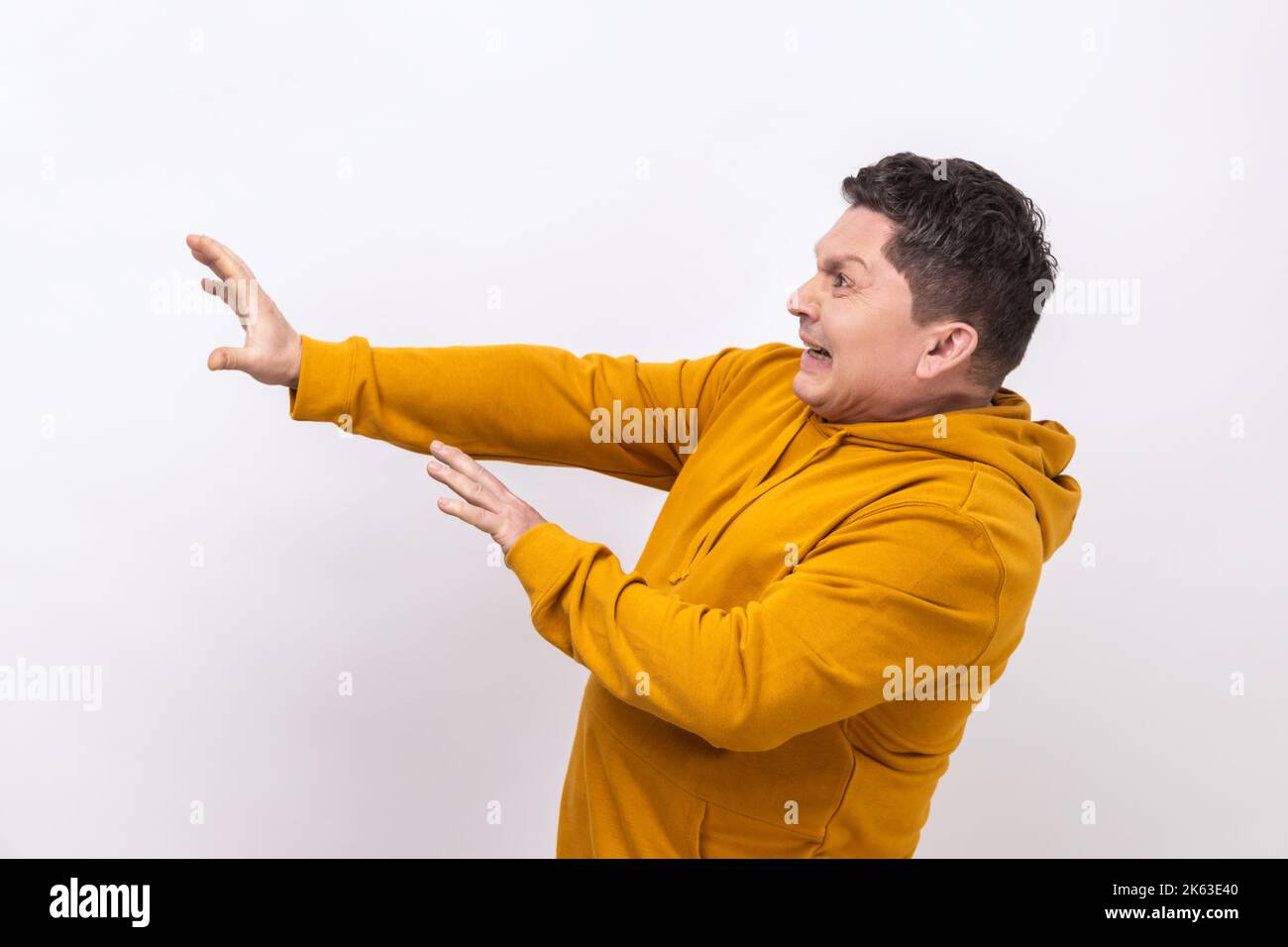 Seitenansicht eines verängstigten Mannes, der mit einem Angst- oder Sorgengesicht steht, auf die Kamera schaut und mit den Händen blockiert, mit einem Hoodie im urbanen Stil. Innenaufnahme des Studios isoliert auf weißem Hintergrund. Stockfoto