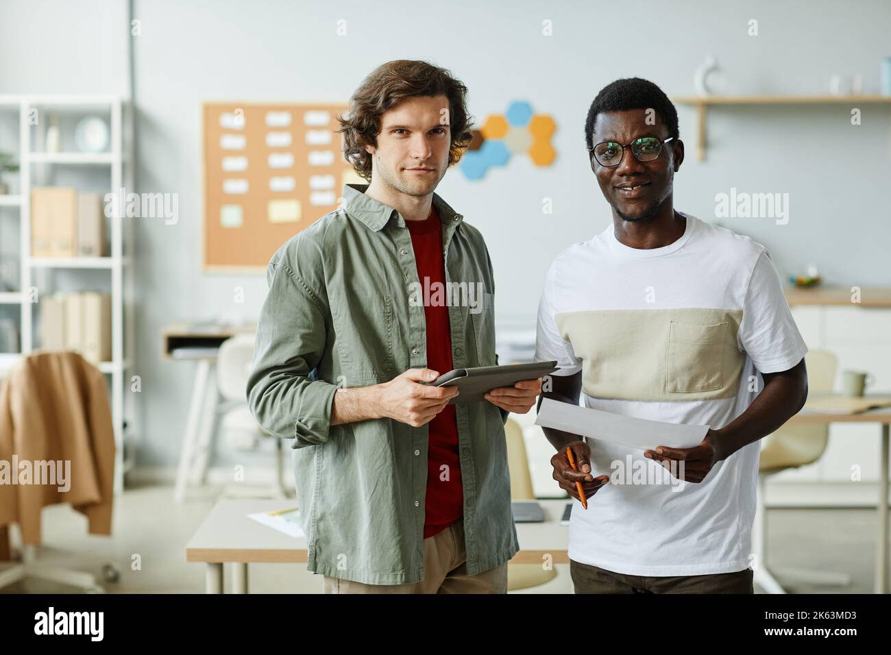 Porträt von zwei jungen IT-Profis, die im Büro auf die Kamera schauen und Dokumente festhalten Stockfoto