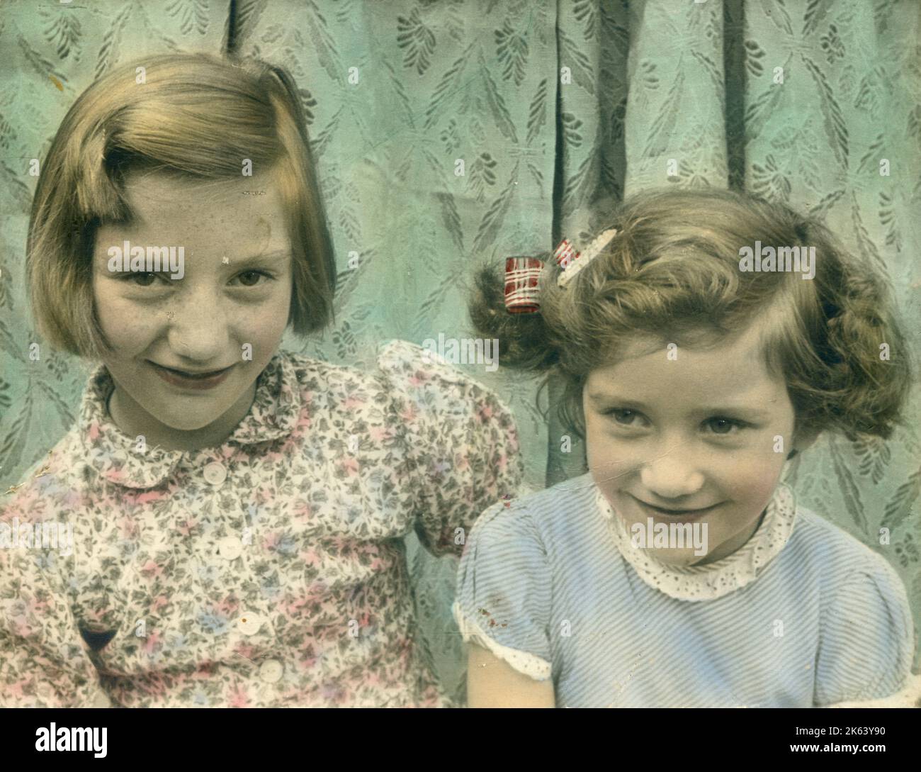 Entzückende Farbaufnahme von zwei kleinen Mädchen, möglicherweise Schwestern, die zusammen sitzen. Datum: ca. 1950 Stockfoto