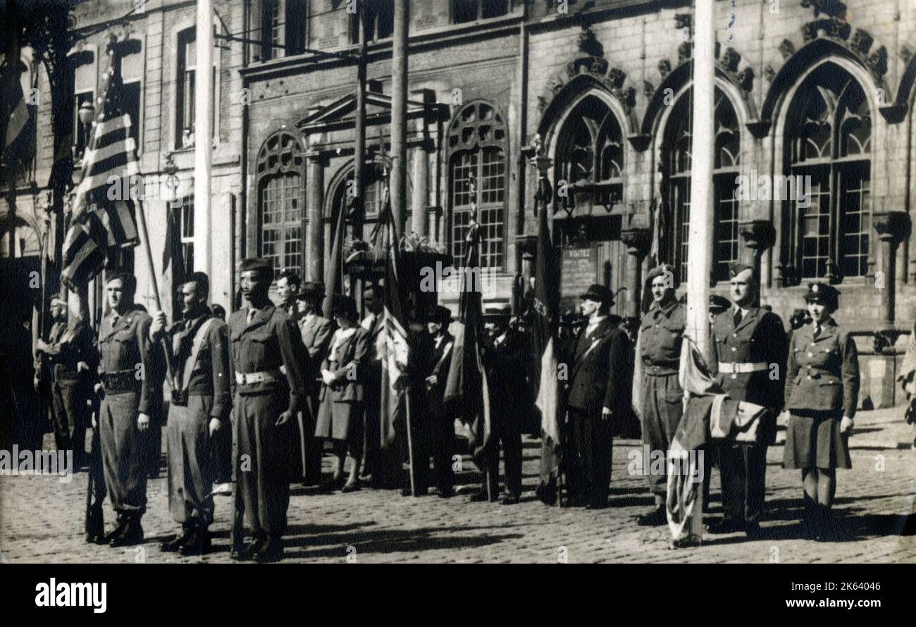 Britische und amerikanische Truppen, die mit Fahnen irgendwo in Belgien oder Frankreich bei einer offiziellen Veranstaltung stehen. Stockfoto