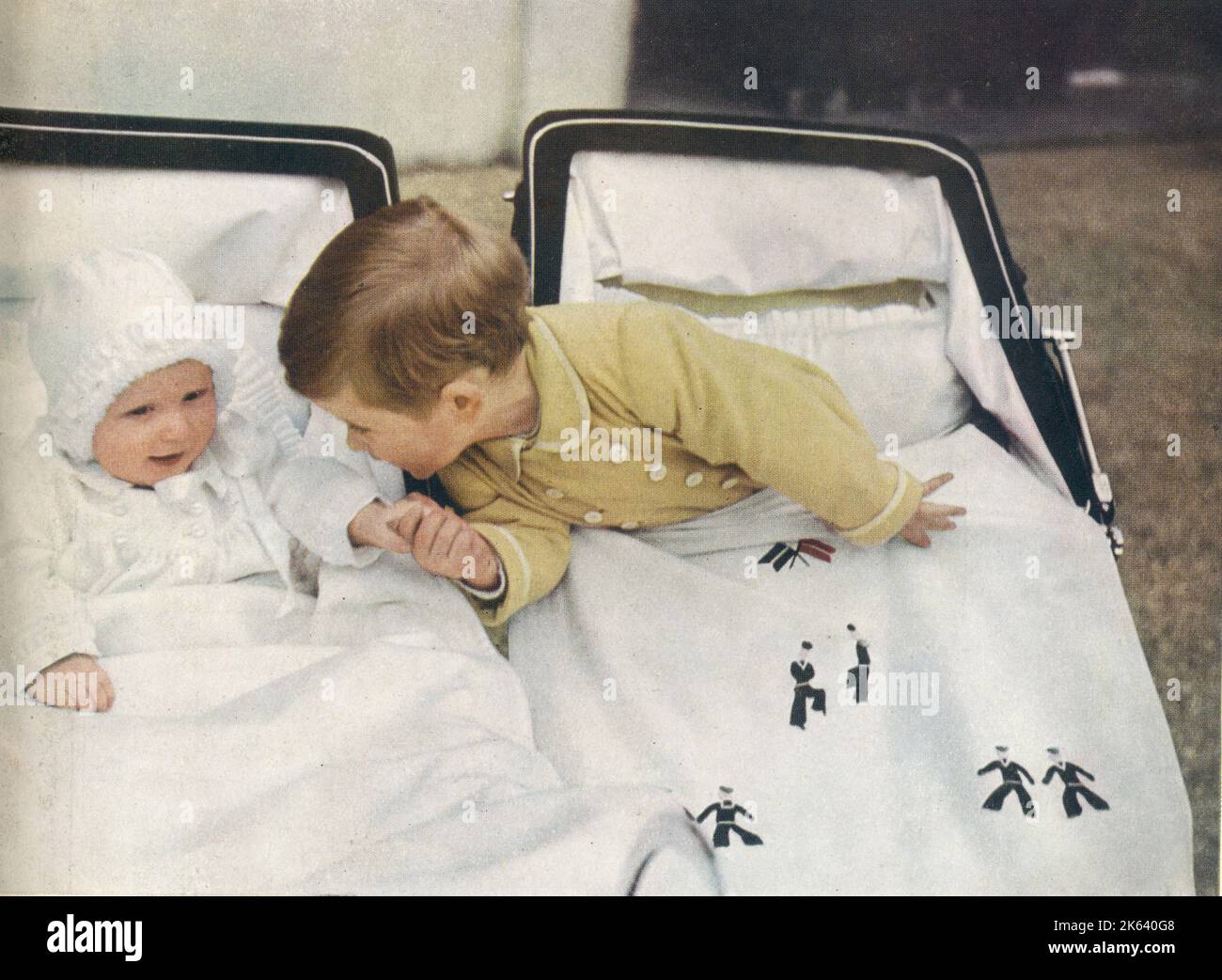Prinz Charles lehnt sich über seinen Kinderwagen, um die Hand seiner kleinen Schwester Prinzessin Anne zu nehmen. Stockfoto