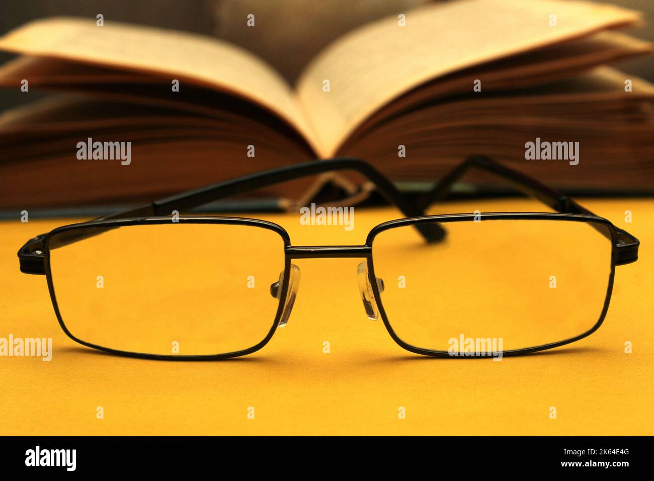 Brille in schwarzem Rahmen auf gelbem Hintergrund. Im Hintergrund ist ein offenes Buch. Welttag des Sehens. Stockfoto