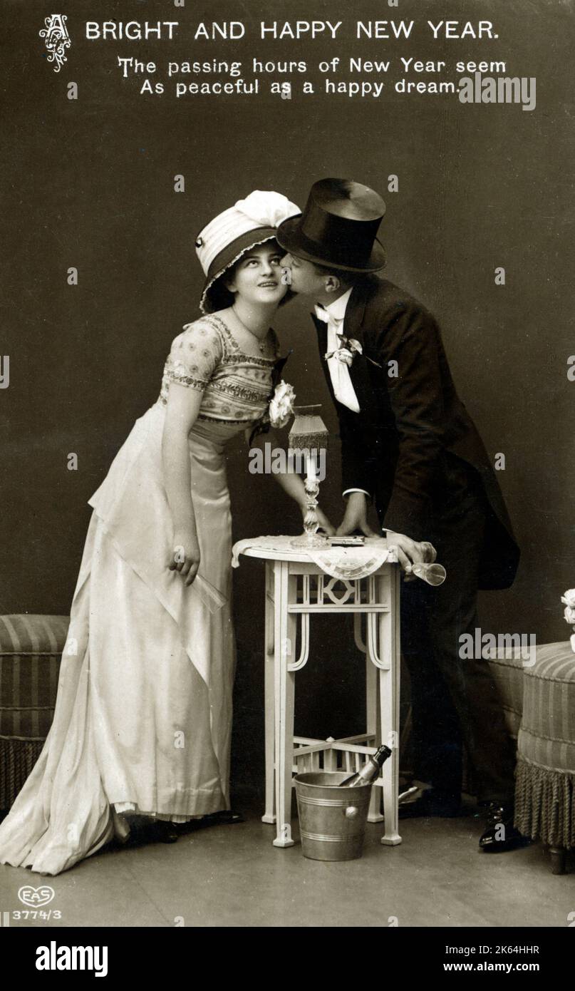 Eine Neujahrskarte mit einem jungen deutschen Paar, das sich eine Flasche Sekt und einen Kuss teilt (über einem kleinen Beistelltisch!) - Die vergehenden Stunden des neuen Jahres scheinen - so friedlich wie ein glücklicher Traum. Datum: 1914 Stockfoto