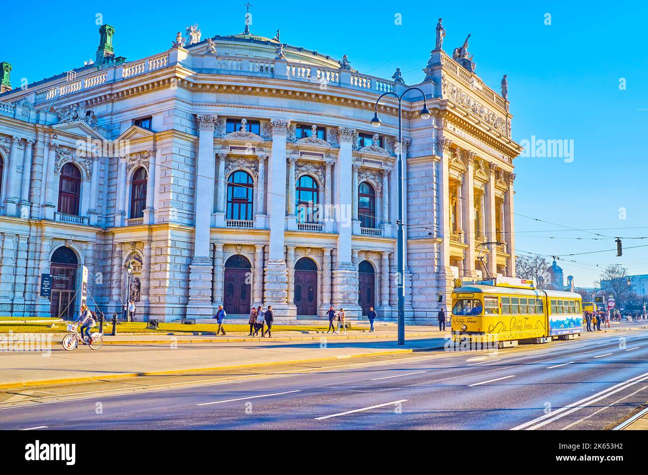 WIEN, ÖSTERREICH - 17. FEBRUAR 2019: Die gelbe Straßenbahn im Retro-Stil fährt am 17. Februar i entlang der Ringstraße mit dem herausragenden historischen Burgtheater Stockfoto
