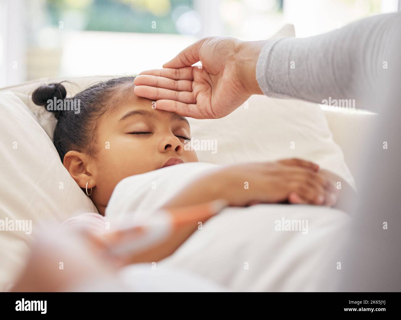 Krankes kleines Mädchen im Bett, während besorgte Mutter ein Thermometer benutzt, um ihre Temperatur zu überprüfen. Gemischte Rasse Eltern Gefühl Töchter Stirn. Hispanisch Stockfoto